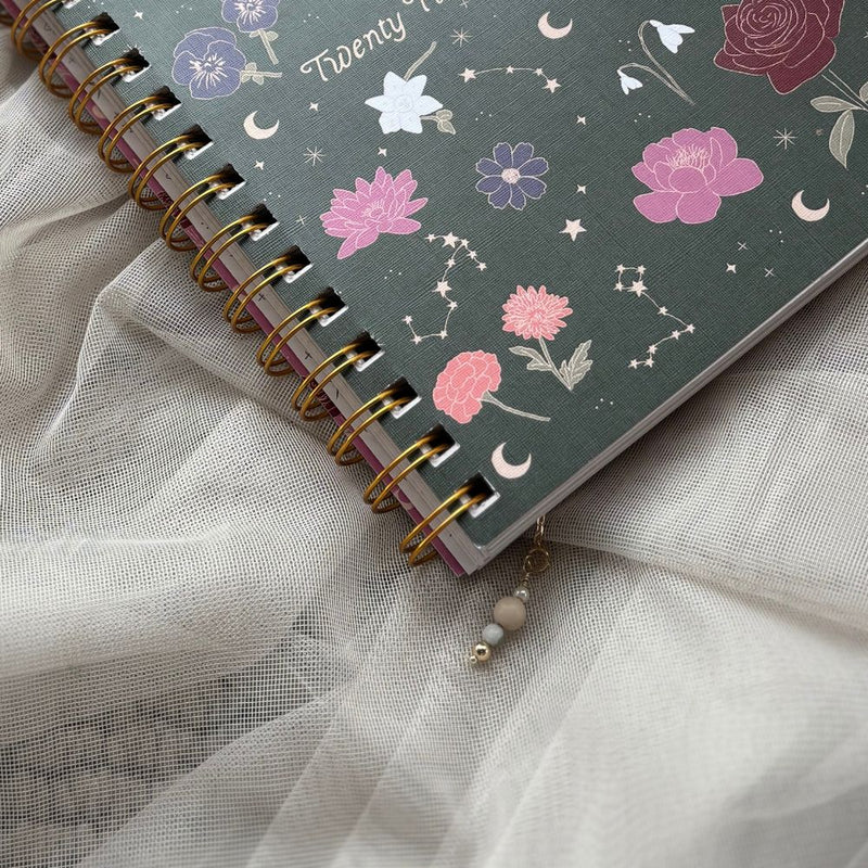 Green diary with floral and celestial design on a light fabric background