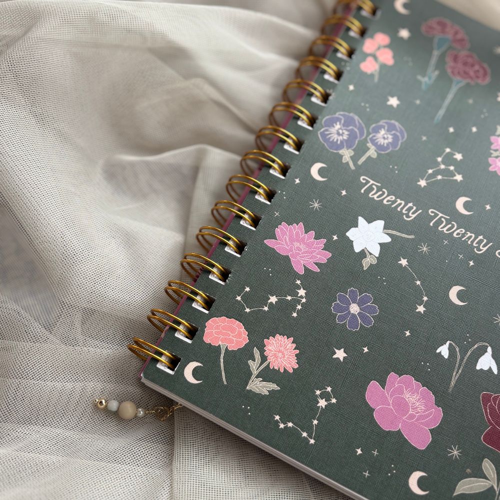Spiral-bound planner with floral and celestial design on a light fabric background