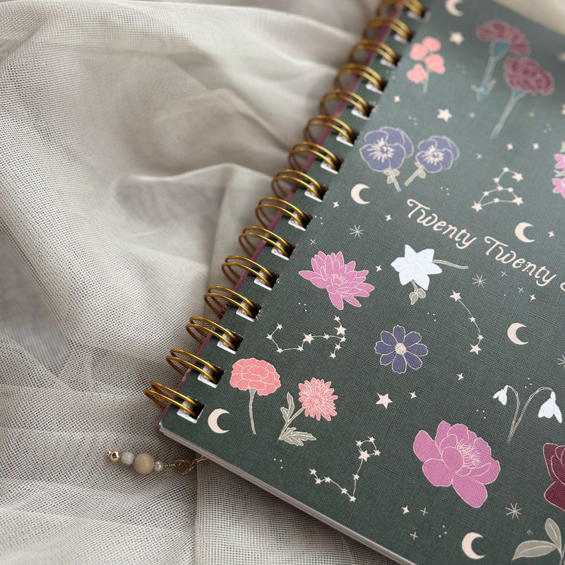 Spiral-bound planner with floral and celestial design on a light fabric background
